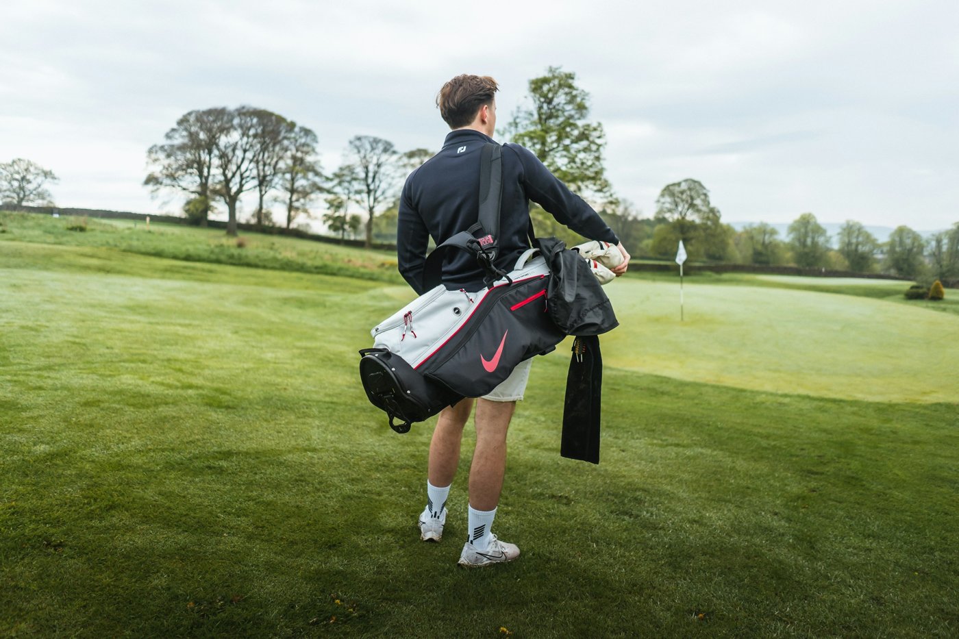 Golfer carrying a golf bag across a green course